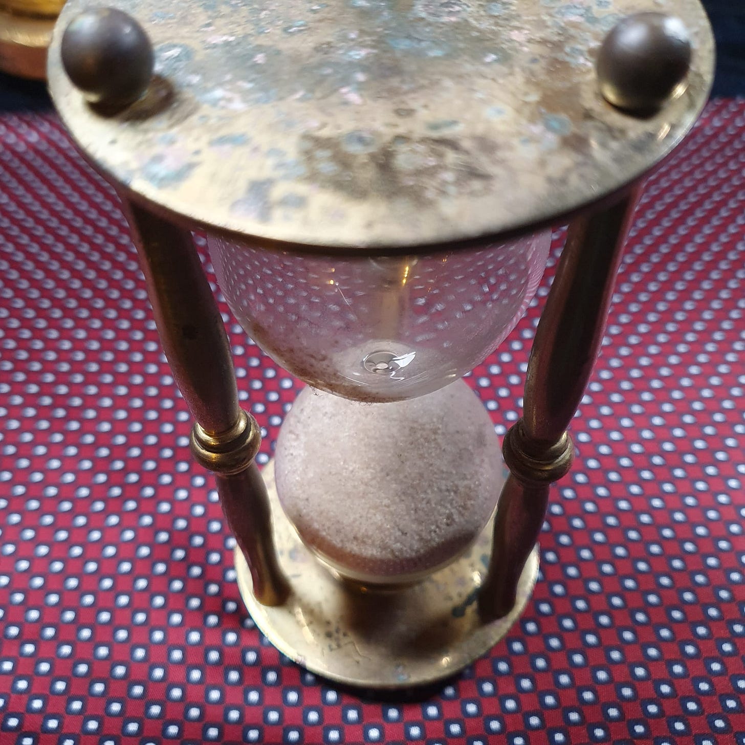 Vintage brass hourglass with patina and sand timer glass on patterned cloth - symbolic object representing time, mortality and gothic atmosphere in tarot and folklore discussion. Vintage brass hourglass with patina and sand timer glass on patterned cloth - symbolic object representing time, mortality and gothic atmosphere in tarot and folklore discussion.