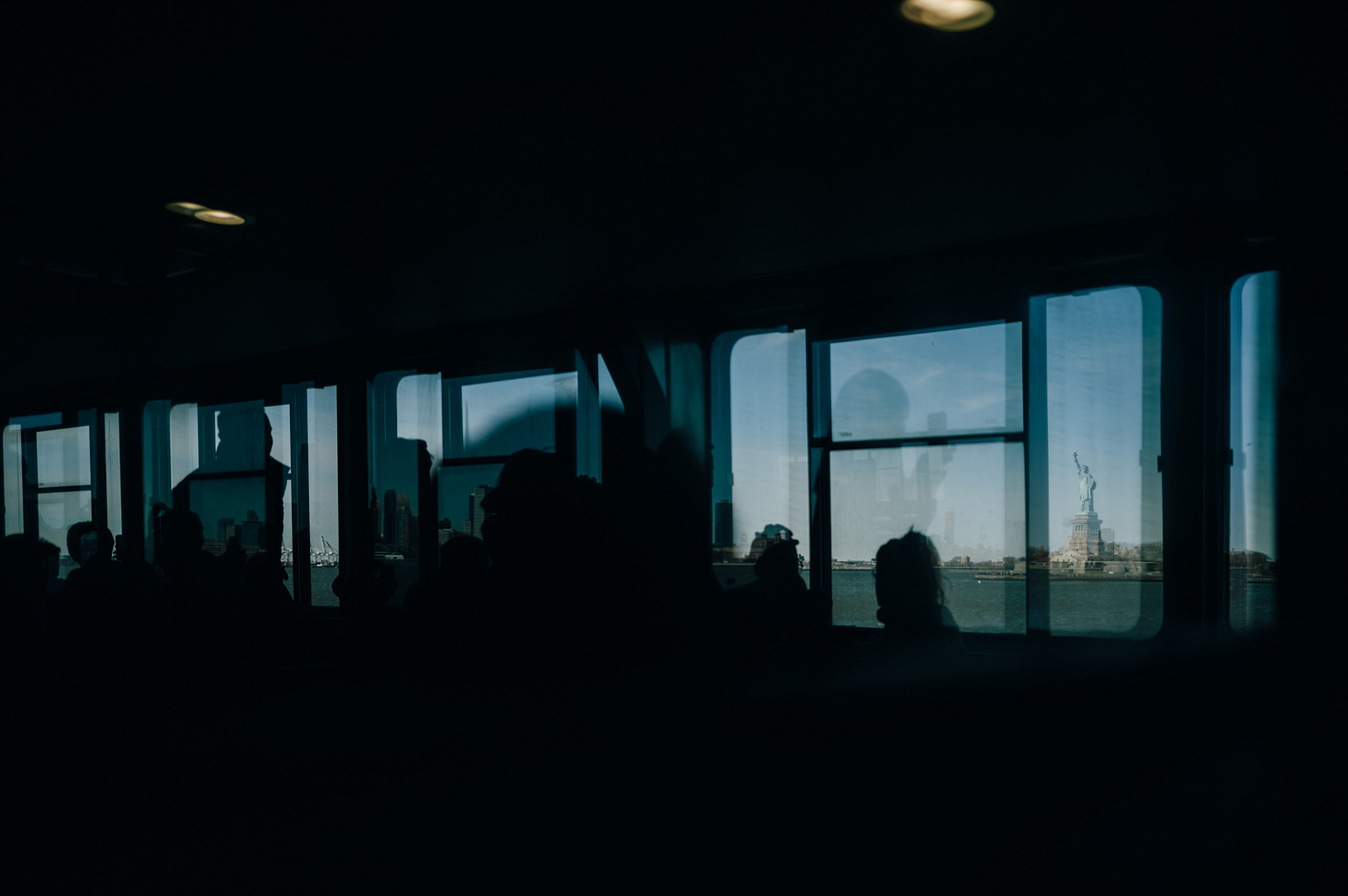 Passengers silhouetted in the dark cabin of the Staten Island Ferry with the Statue of Liberty visible small through the far right window, New York Harbor.