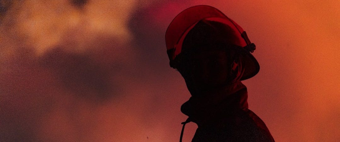 A firefighter stands in front of a fiery sky. A firefighter stands in front of a fiery sky.