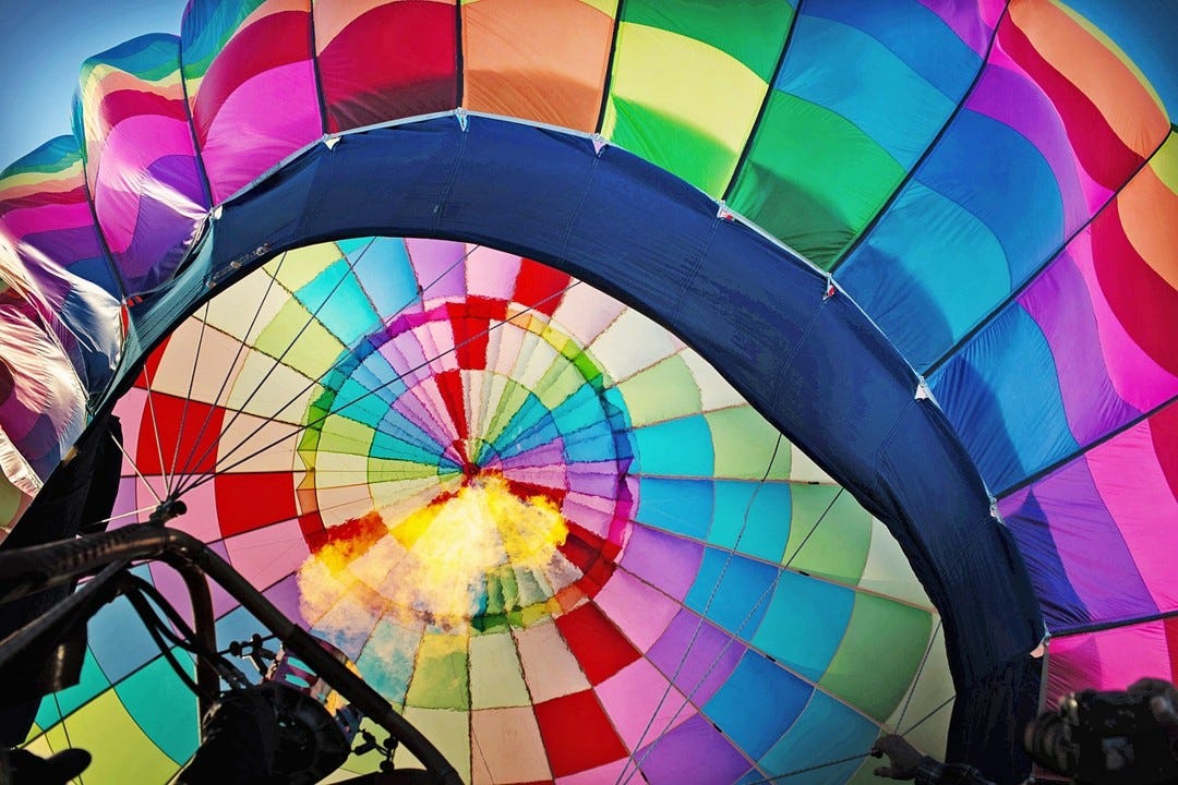 A colourful hot air balloon canopy seen from below with a lit flame surging upwards from a burner.