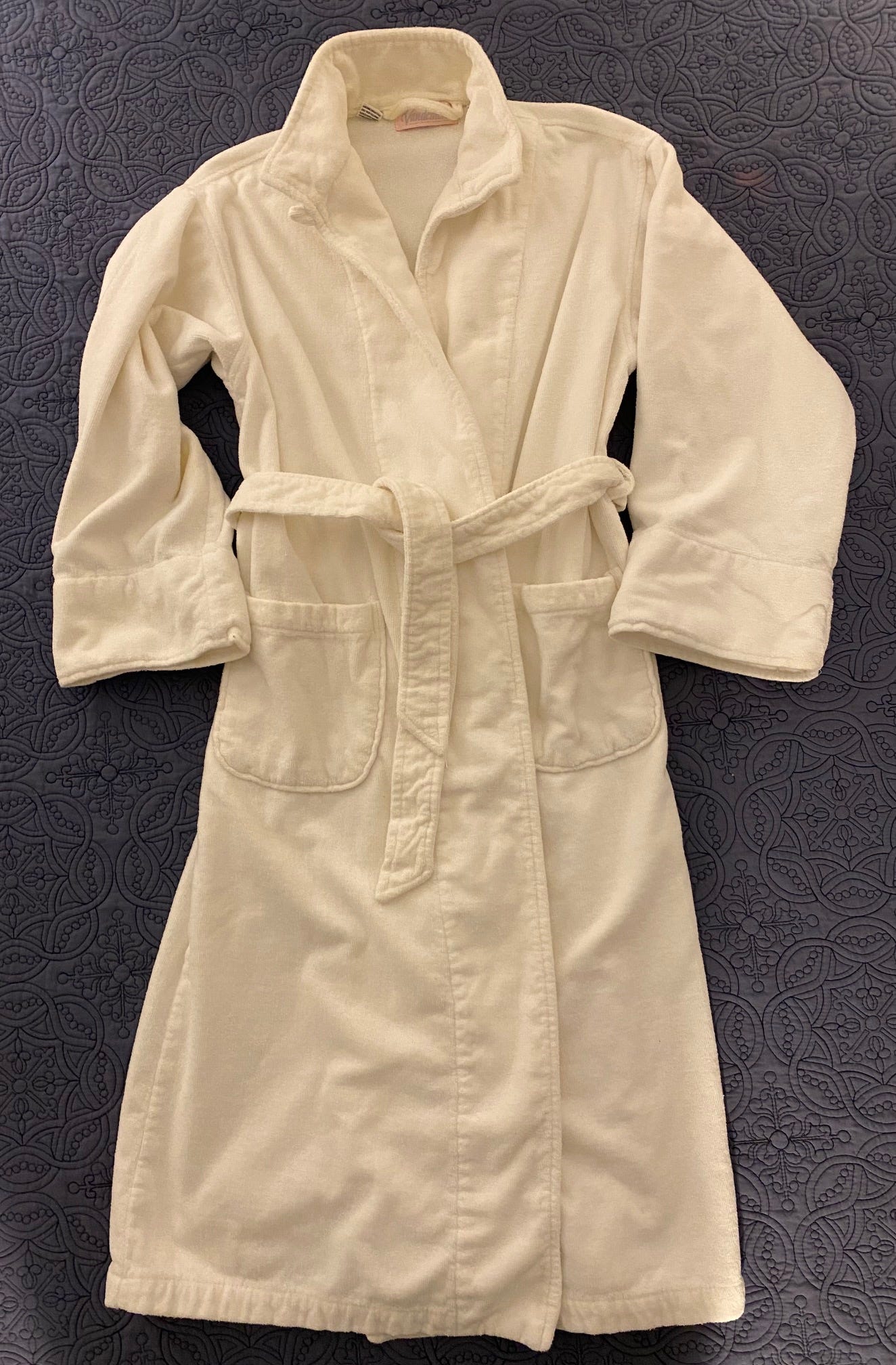 White terry cloth robe spread out on navy blue bedspread. Tied around waist with terry cloth robe belt. 
