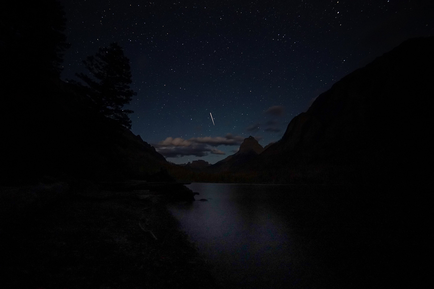 Starry night sky with mountains, lake, and comet.