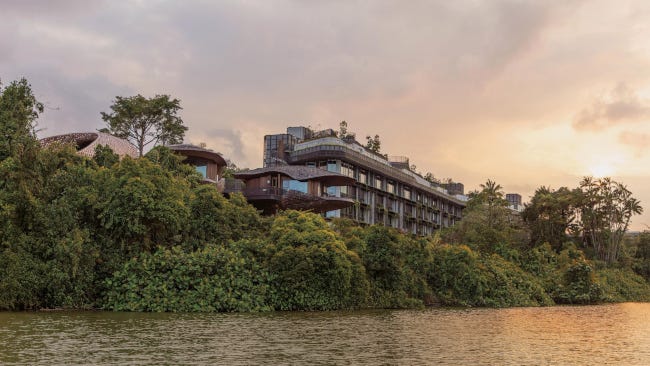 Un merveilleux hôtel de couleur pierre nich dans la jungle, sur un promontoire surplombant un lac au soleil couchant
