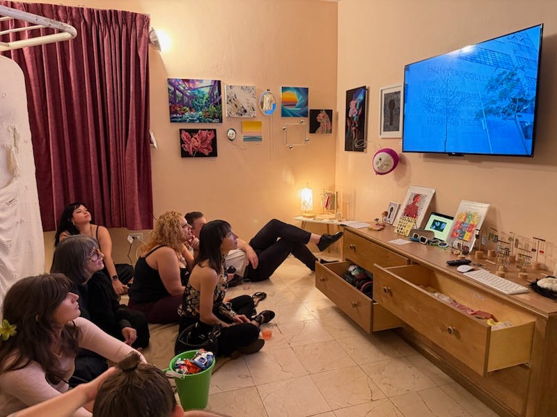 viewers sit on the floor watching a TV surrounded by art works