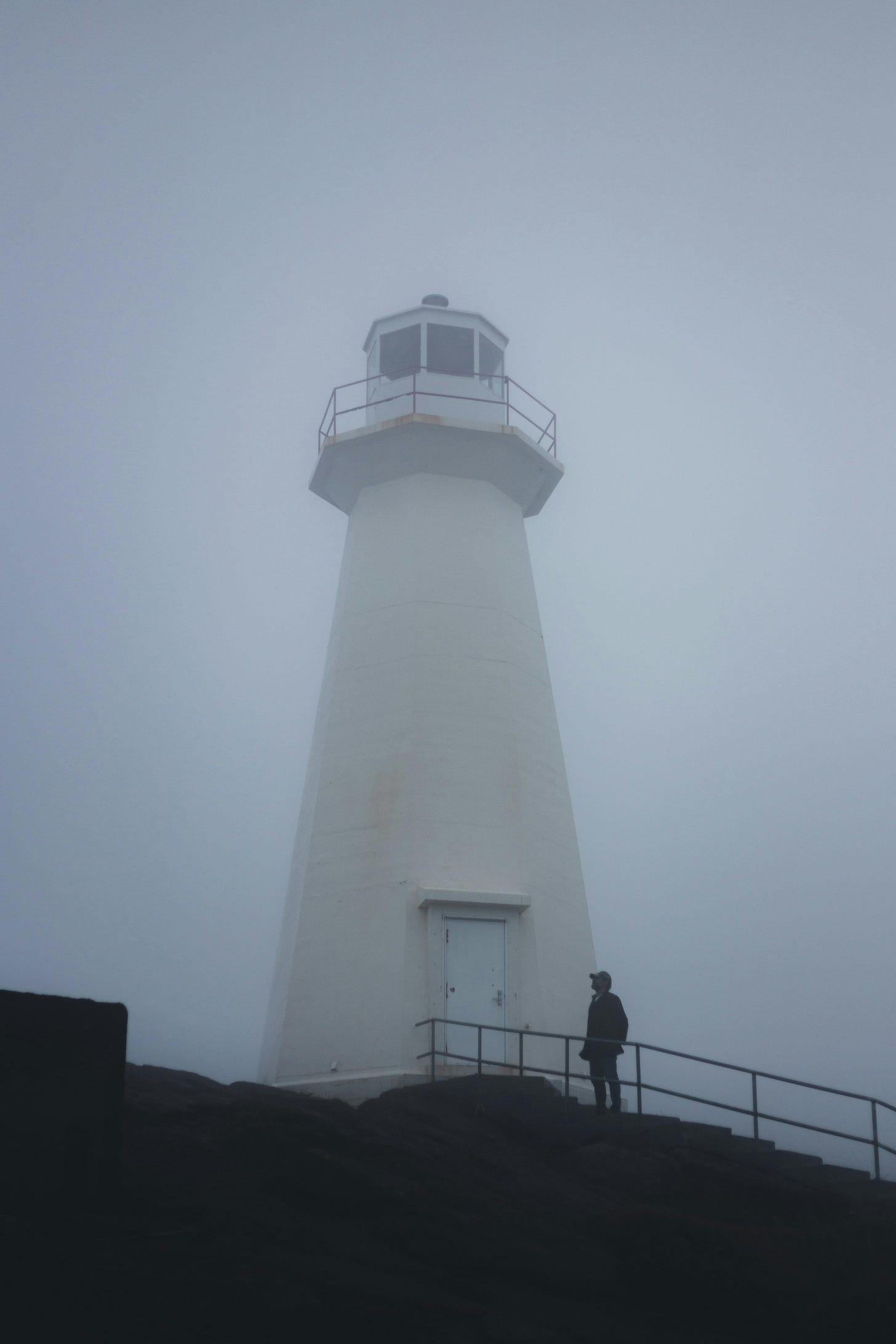 A lighthouse emerging through heavy fog, steady and solitary.