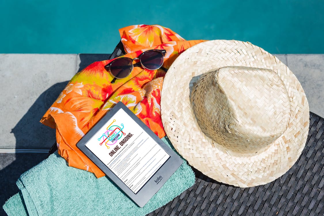 towel, hat, sunglasses, tropical shirt and tablet with third space symposium homepage by a pool