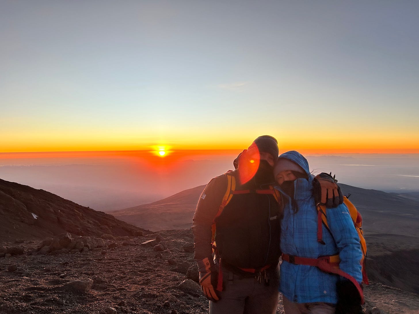 a couple posing on a mountain in front of the sunrise