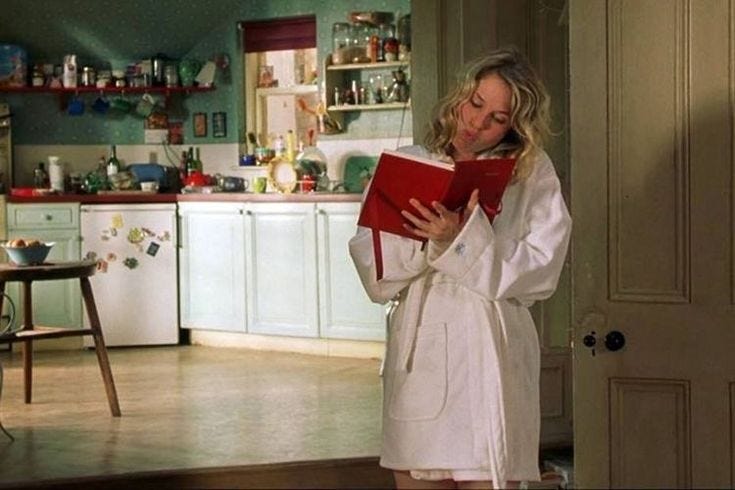 This may contain: a woman in a bathrobe reading a red book while standing in a kitchen