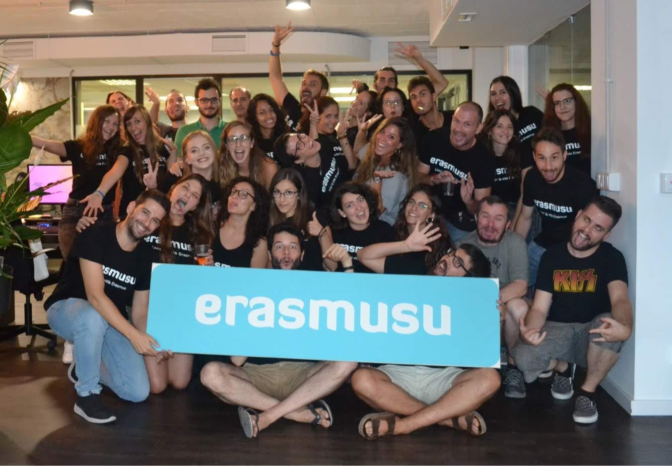 Group photo of the Erasmusu team smiling and posing together indoors while holding a large blue Erasmusu sign.