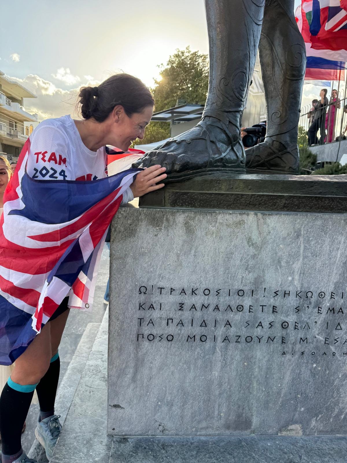 Anna Brown kissing the foot of a statue in modern day Sparta after finishing the Spartathlon