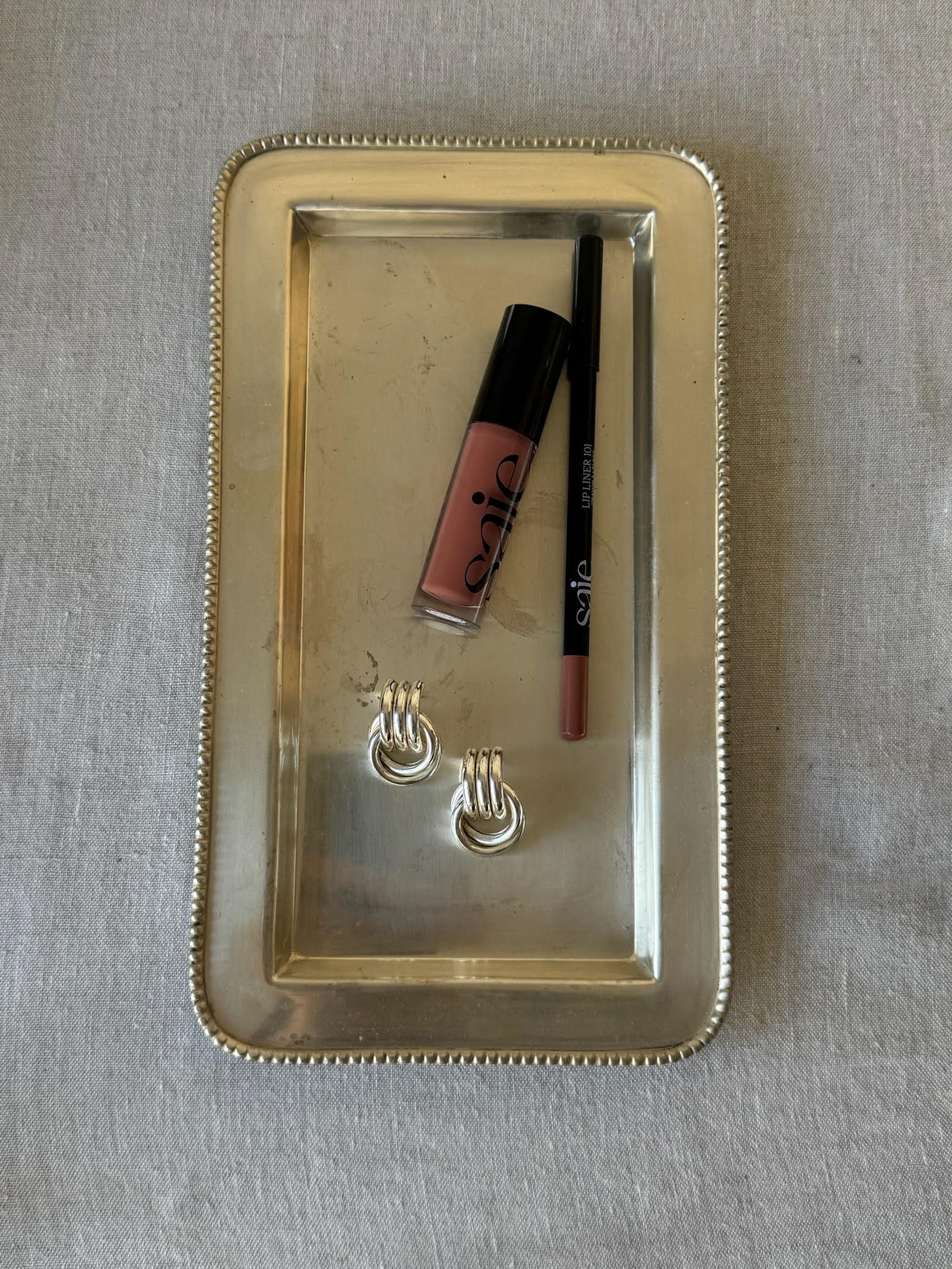 Saie lip gloss and lip line and Heaven Mayhem earrings on a silver tray.
