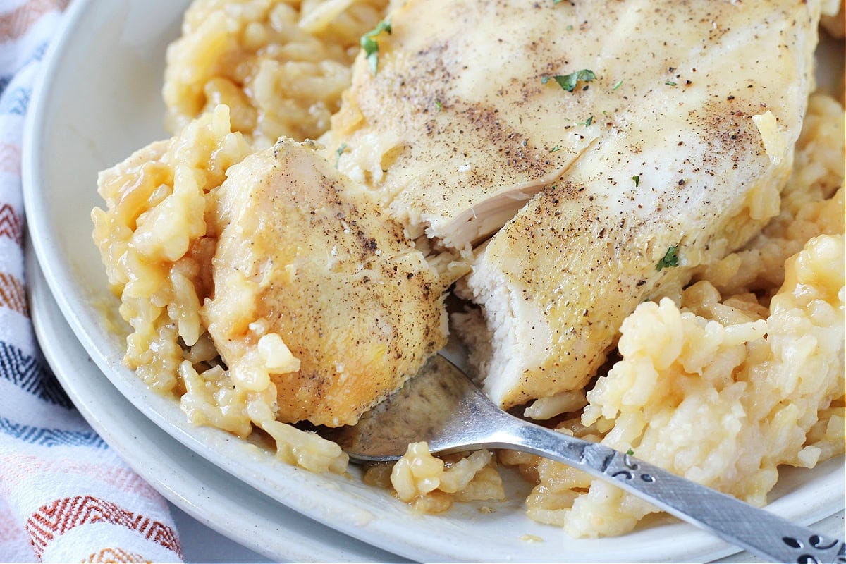 A fork cutting into a chicken breast over creamy rice.