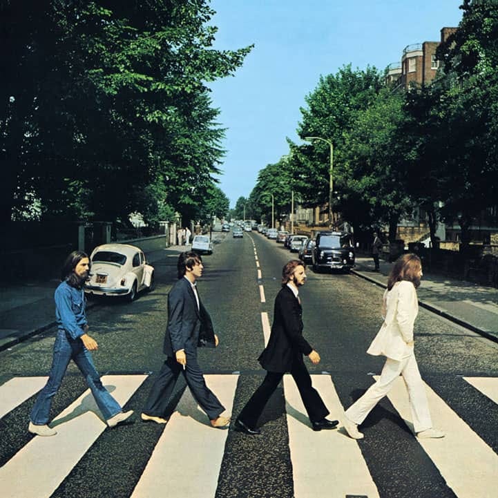 Four men walk across a crosswalk with cars and trees behind them.