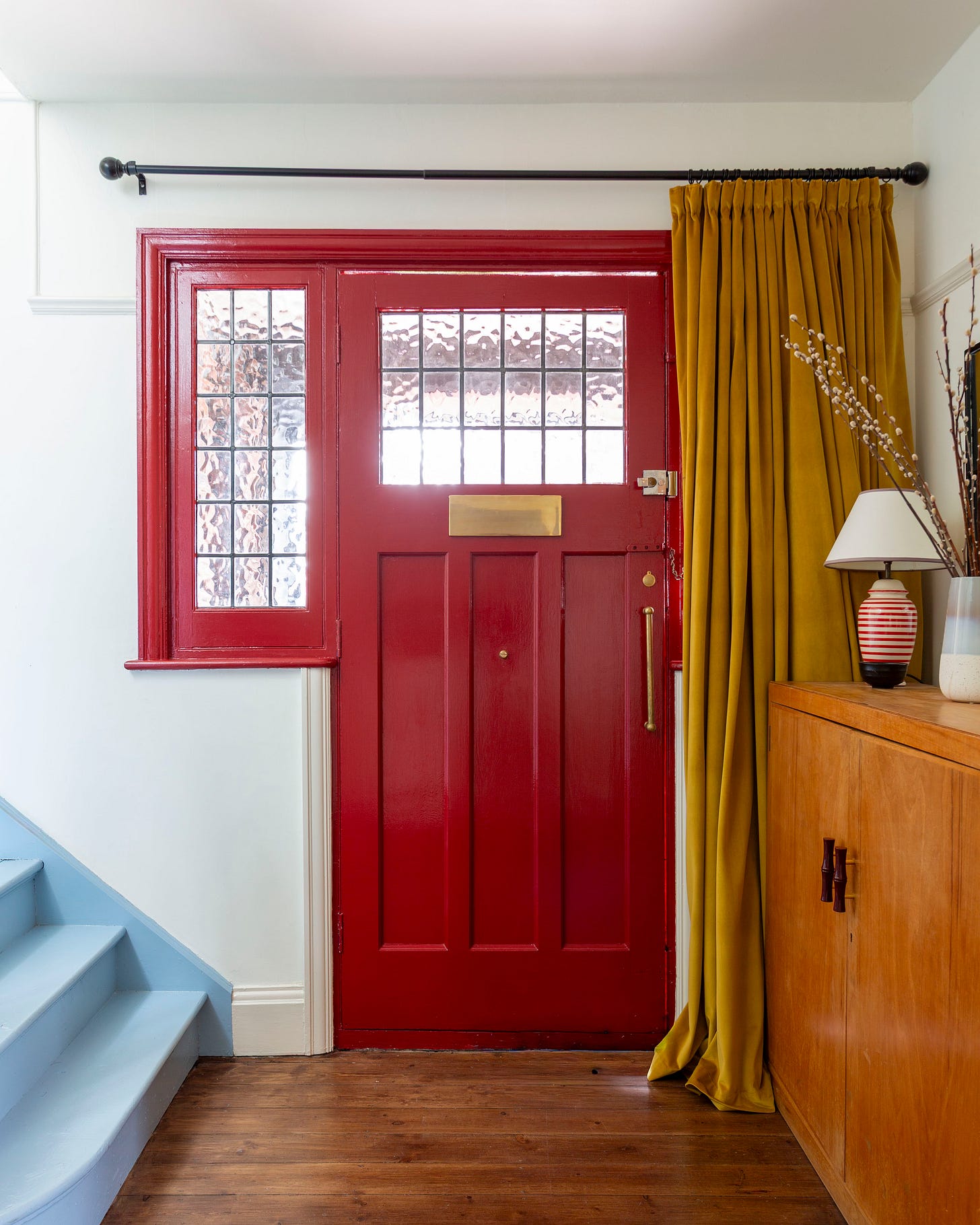 hallway with red door, yellow door curtain and blue stairs. vintage shoe cupboard with lamp on