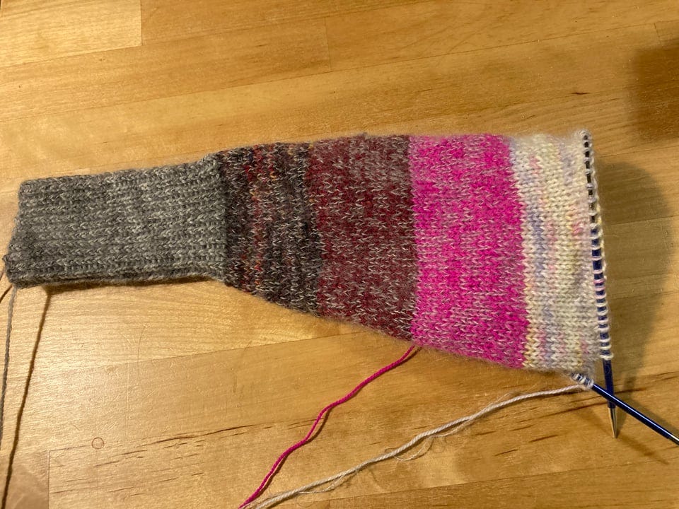 Image of a handknit sweater sleeve in gray, maroon, red, pink, and cream stripes.