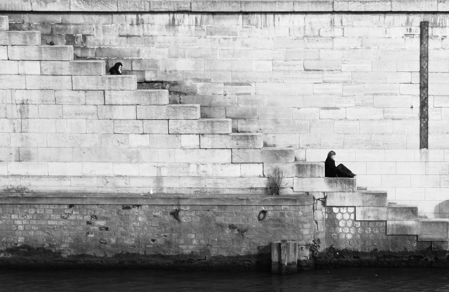 A solitary woman sitting on large stone steps beside a river, surrounded by minimalist architecture - a visual metaphor for introversion and reflective writing. A solitary woman sitting on large stone steps beside a river, surrounded by minimalist architecture - a visual metaphor for introversion and reflective writing.