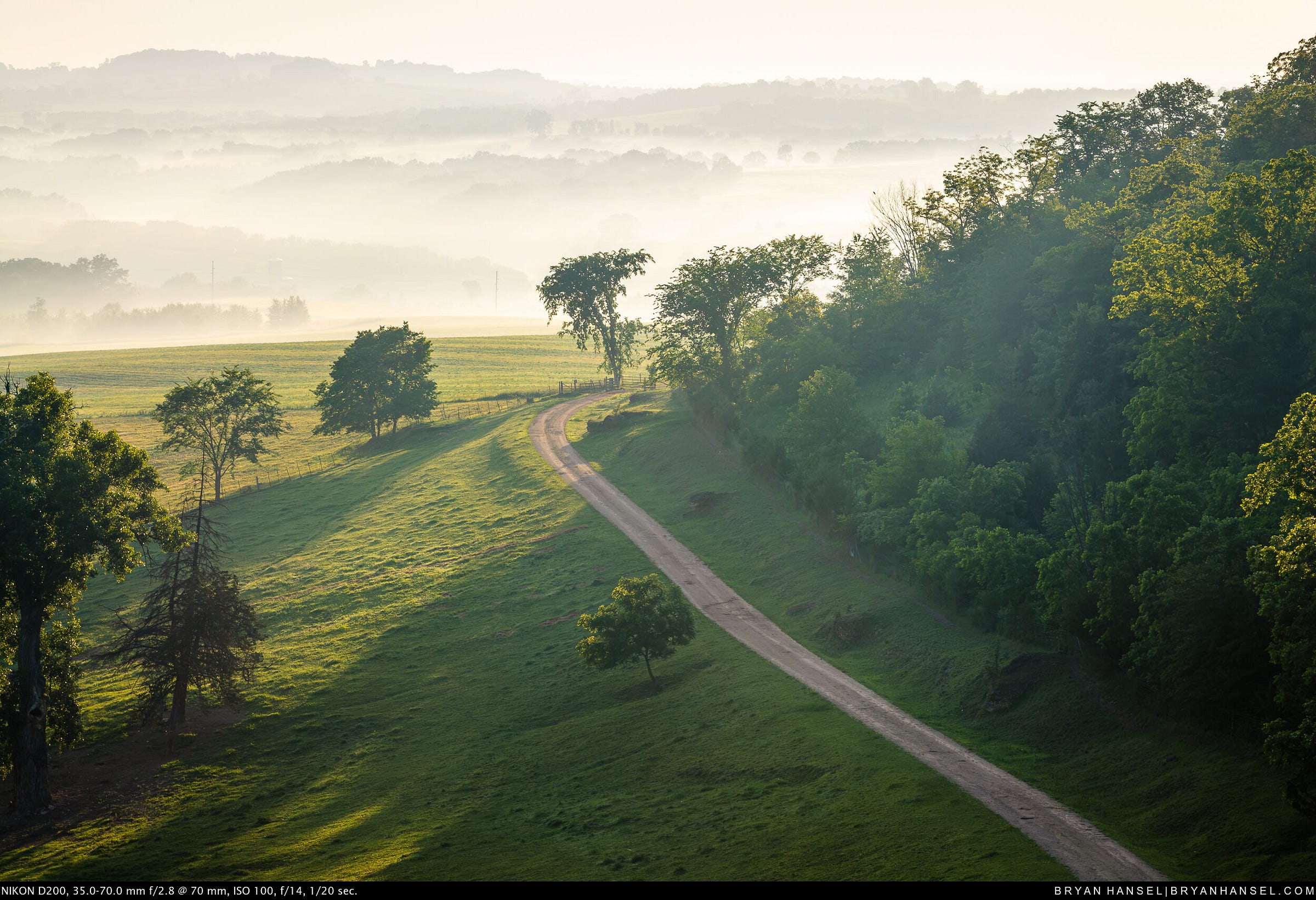A Iowa farm field covered in early morning mist leading out to hills covered in mist.