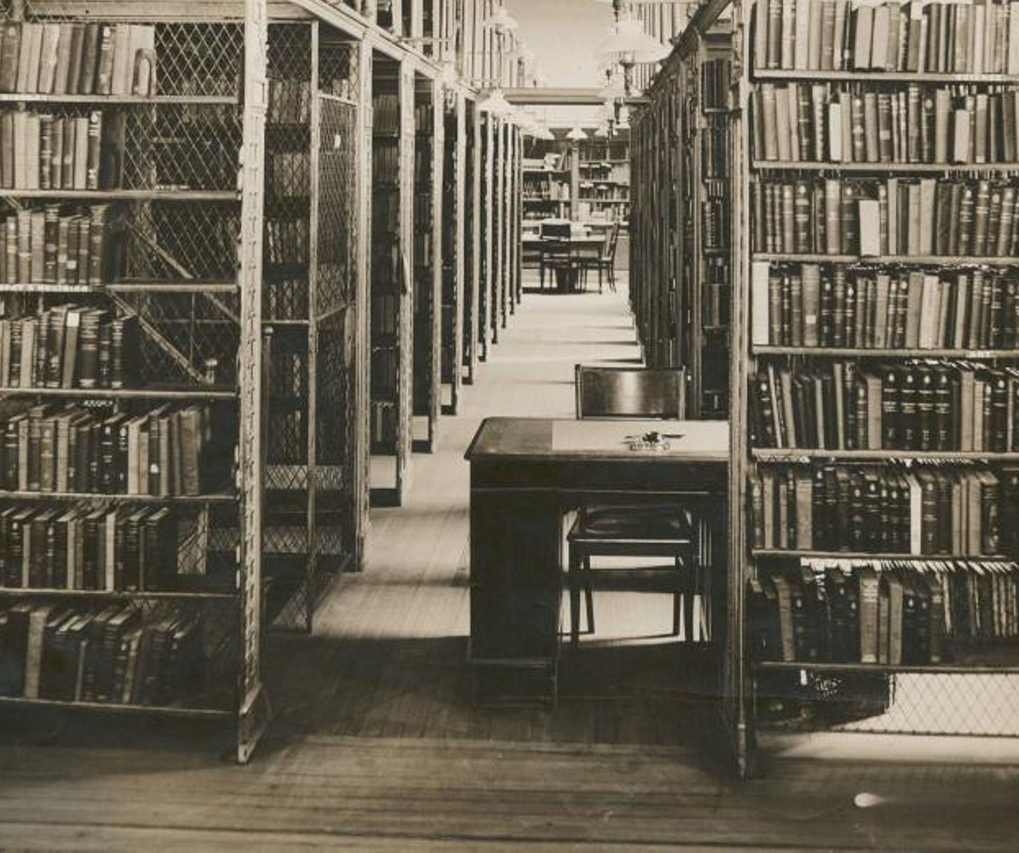 A photo of rows of books and a desk inside a building.