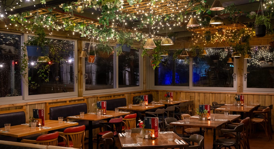 An indoor dining area with wooden seats and a ceiling with green leaves and fairy lights