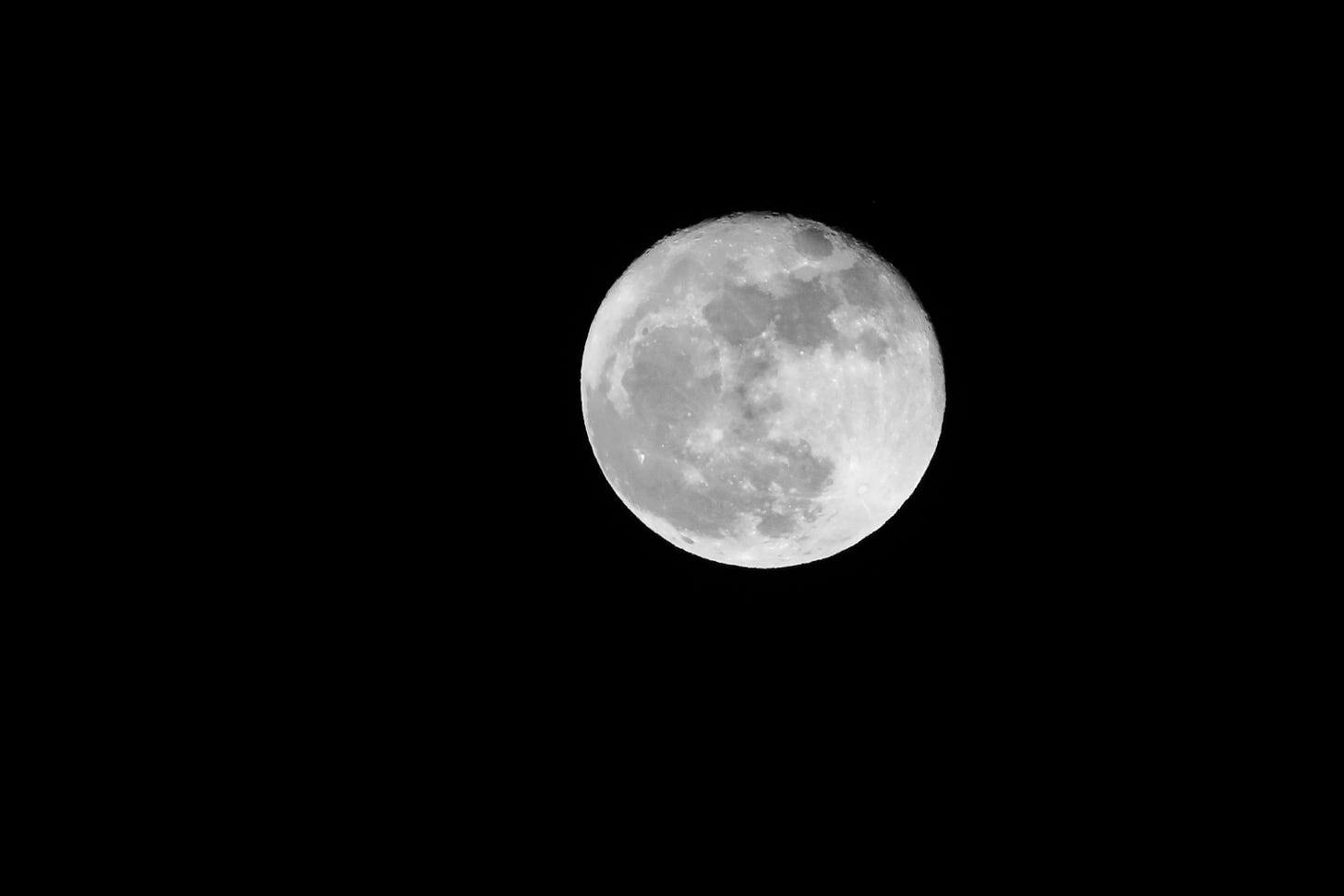Against a completely black sky, the moon, large and round. The moon glows white, with gray craters visible on the surface. Against a completely black sky, the moon, large and round. The moon glows white, with gray craters visible on the surface.