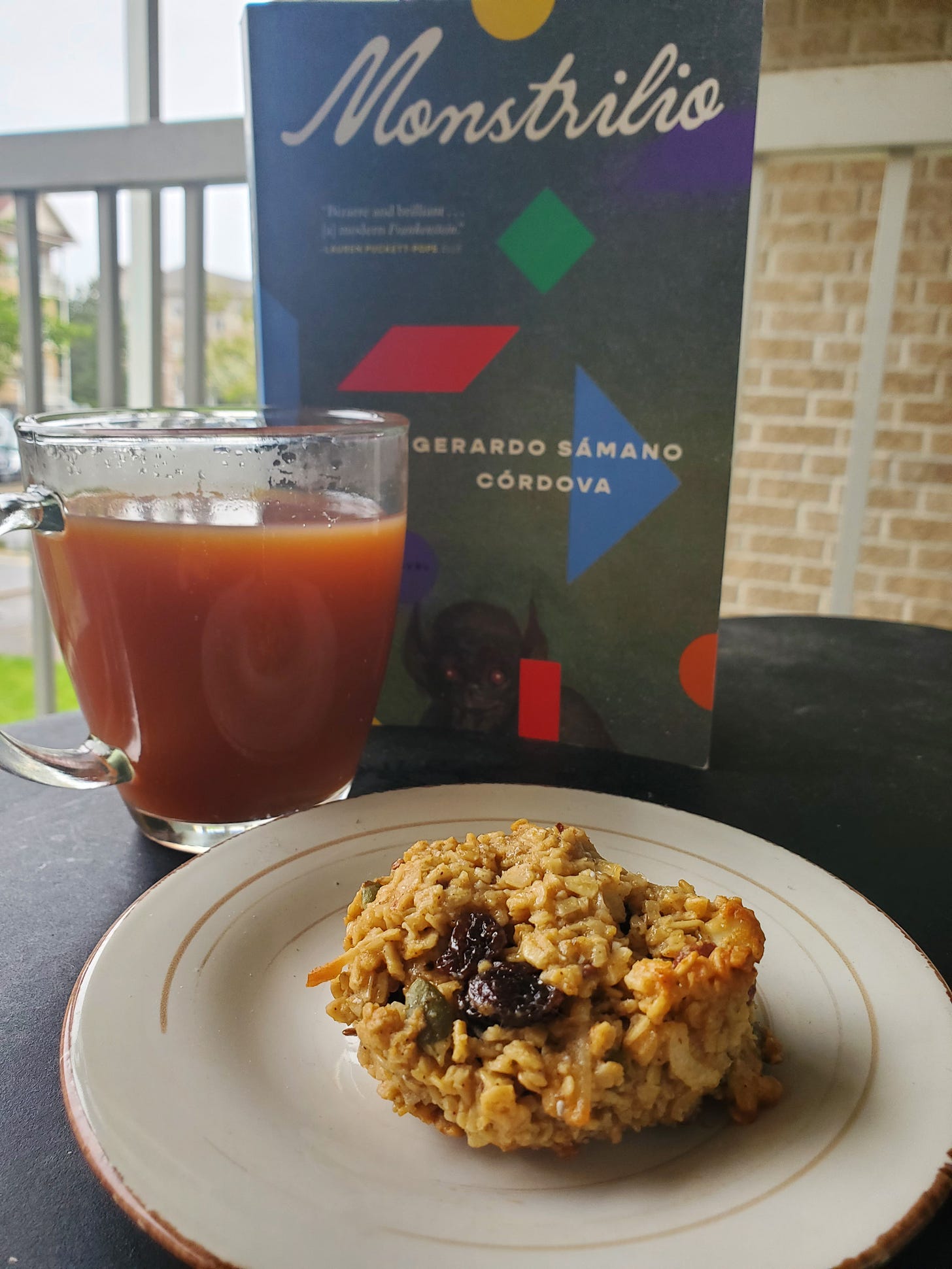 Monstrilio (a novel) stands behind a clear glass mug of tea and a plate with a hearty cookie on it.