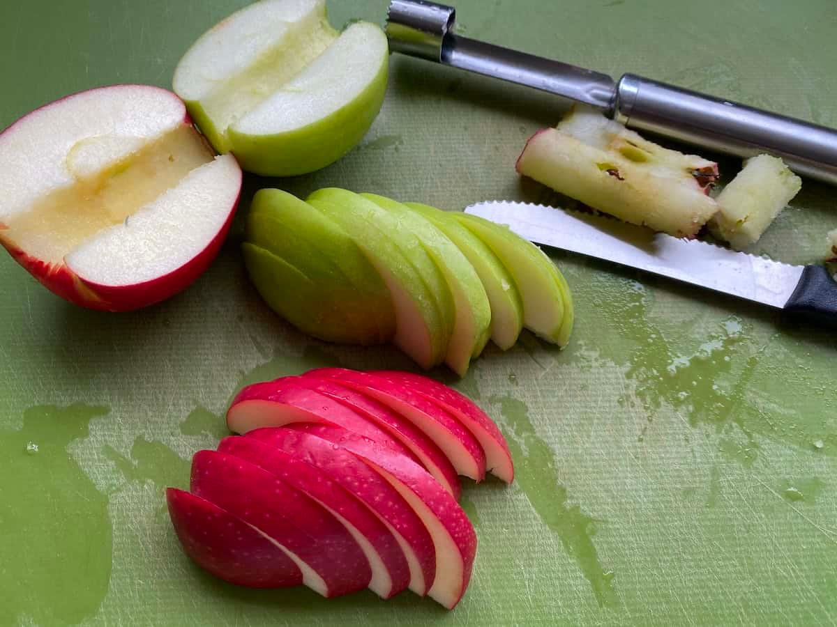 Slices of red and green apples on a green chopping board.