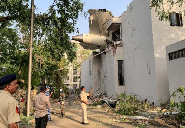 People looking up at the tail of a plane sticking out of an apartment building. People looking up at the tail of a plane sticking out of an apartment building.