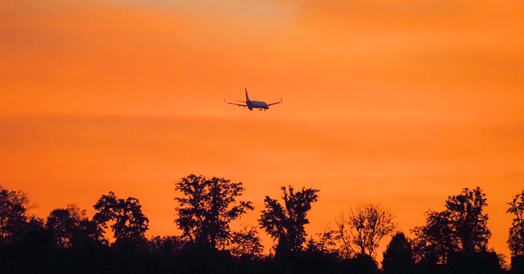 Airplane flying across a vibrant orange sunset sky. Airplane flying across a vibrant orange sunset sky.