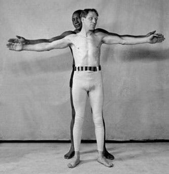 Artistic photo of Jack Johnson, a black boxe, standing behind white boxer Joe Choynski, both fighters with their arms spread wide