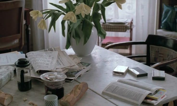 This may contain: flowers in a white vase sitting on top of a table next to books and magazines