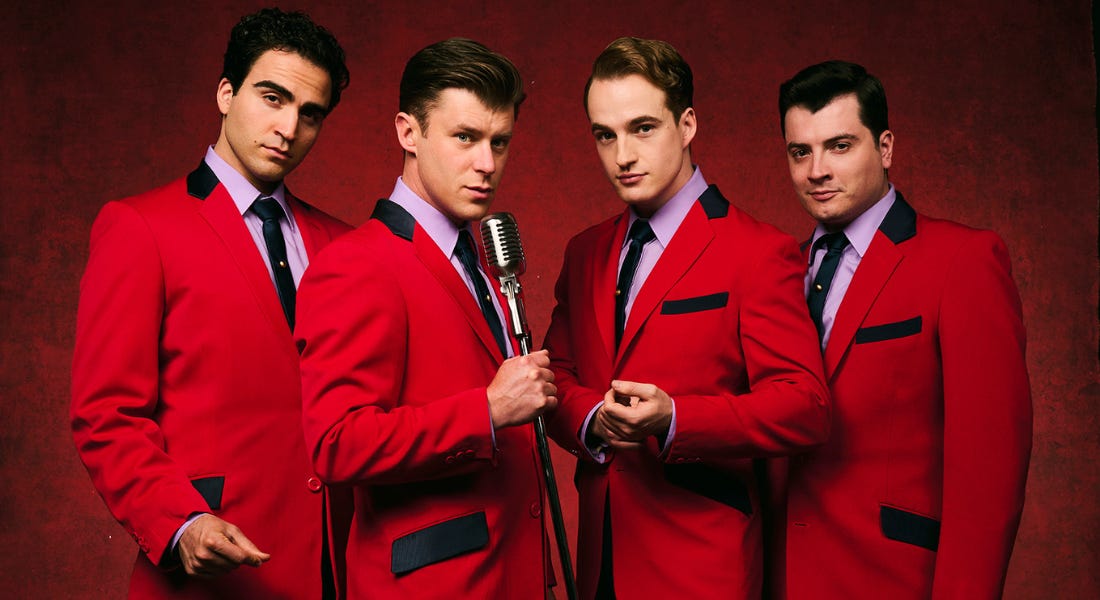 Four men in bright red blazers, purple shirts, and ties against a red background Four men in bright red blazers, purple shirts, and ties against a red background