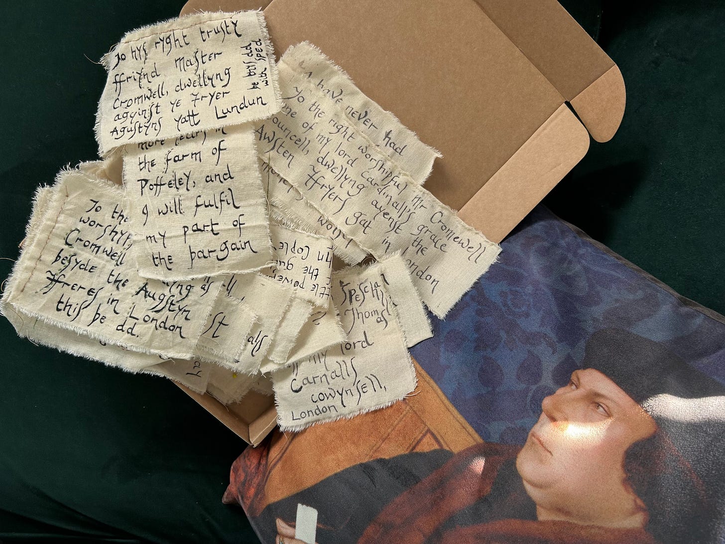 A Thomas Cromwell portrait cushion eyes a box overflowing with inked and stitched representations of his letters