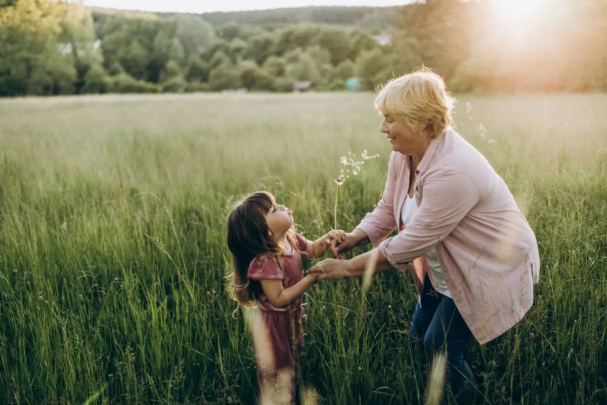 Grandmother and young granddaughter holding hands and looking at each other in a grassy field. Grandmother and young granddaughter holding hands and looking at each other in a grassy field.