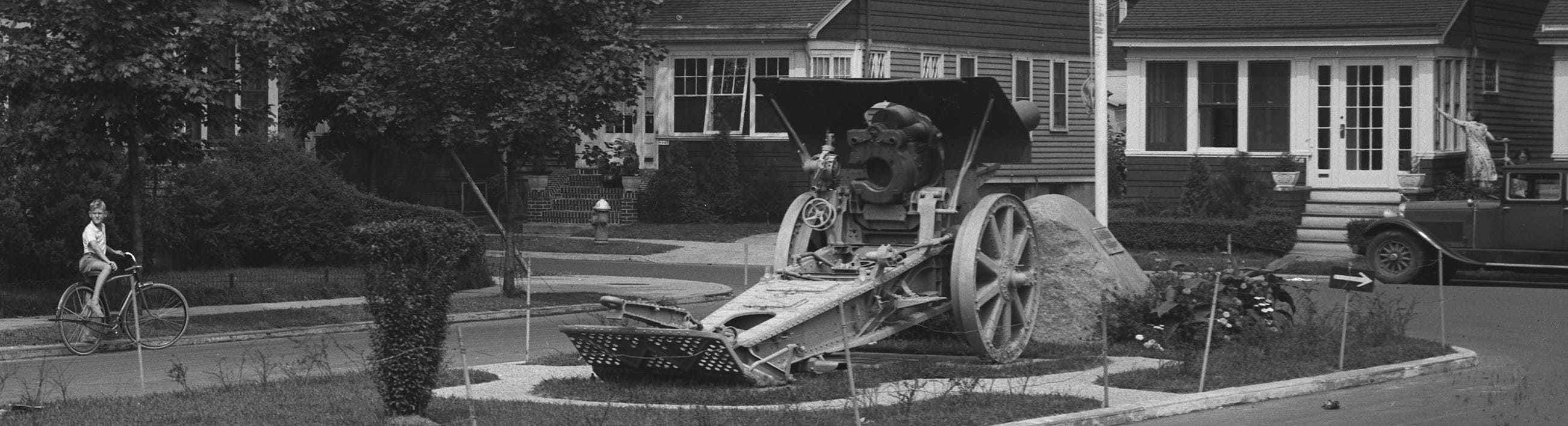 Image is a photograph showing a boy on a bike by the howitzer at Whiting Square.