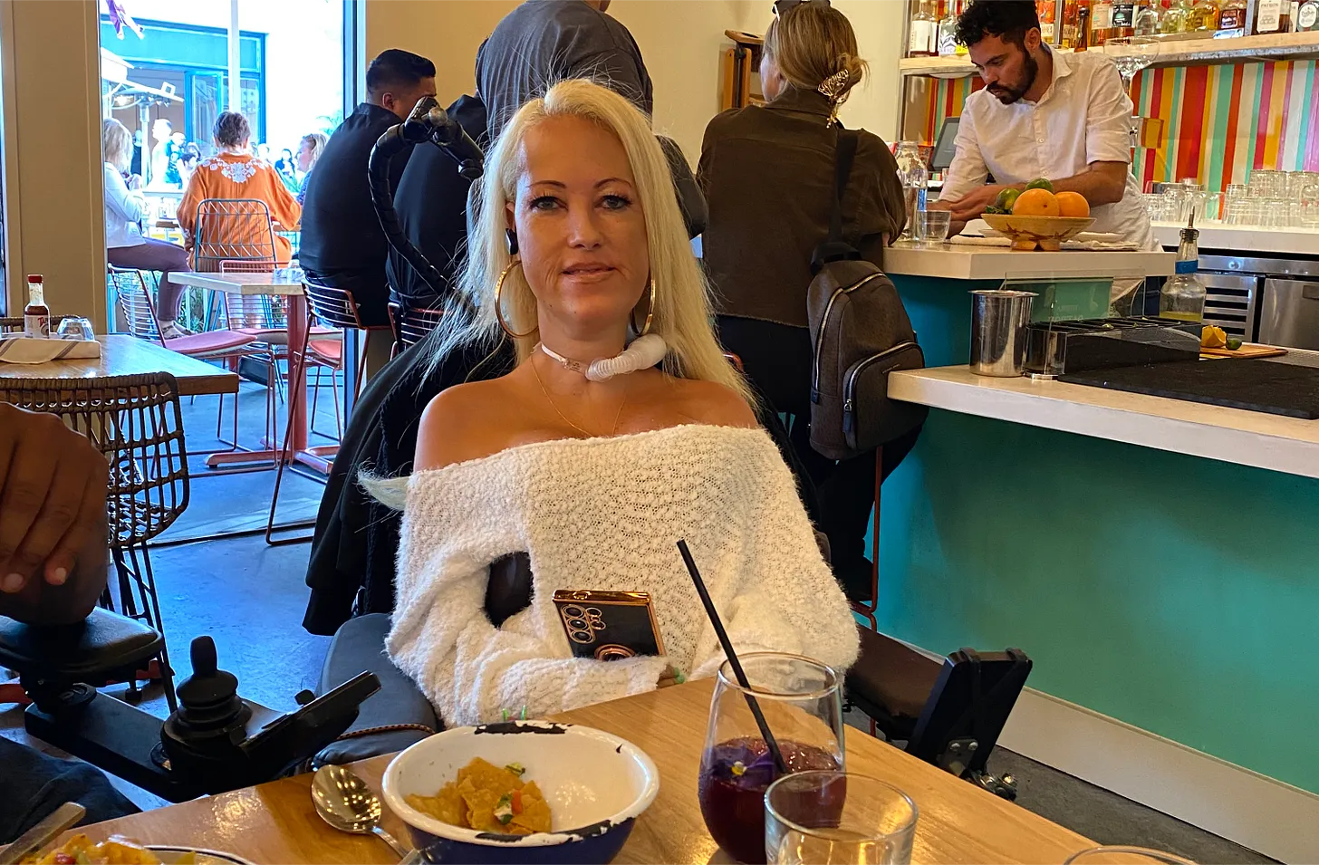 A well-dressed lady in a wheelchair with a drink in front of her in a Mexican restaurant setting. A well-dressed lady in a wheelchair with a drink in front of her in a Mexican restaurant setting.