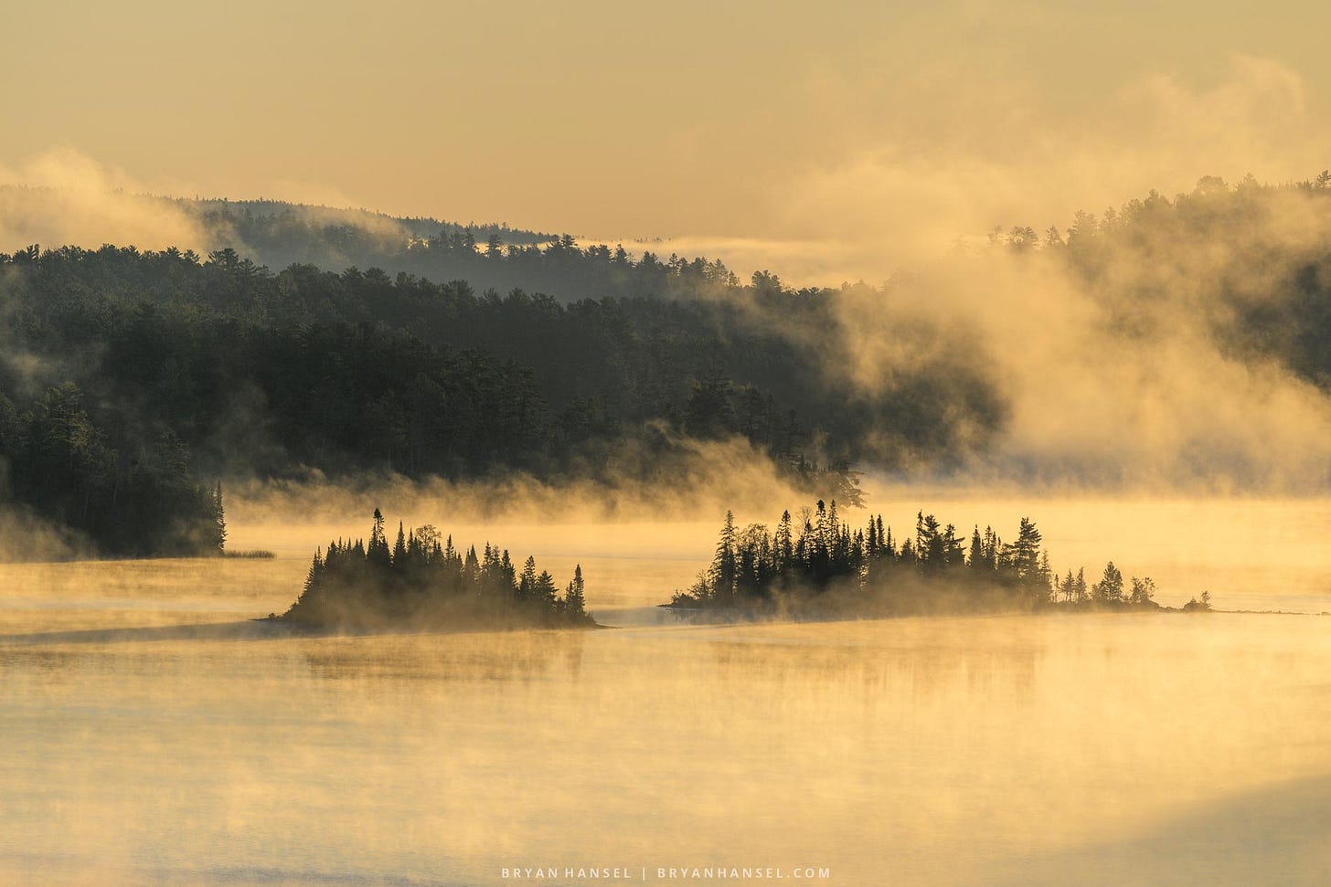 golden orange mist on a lake with two islands on it.
