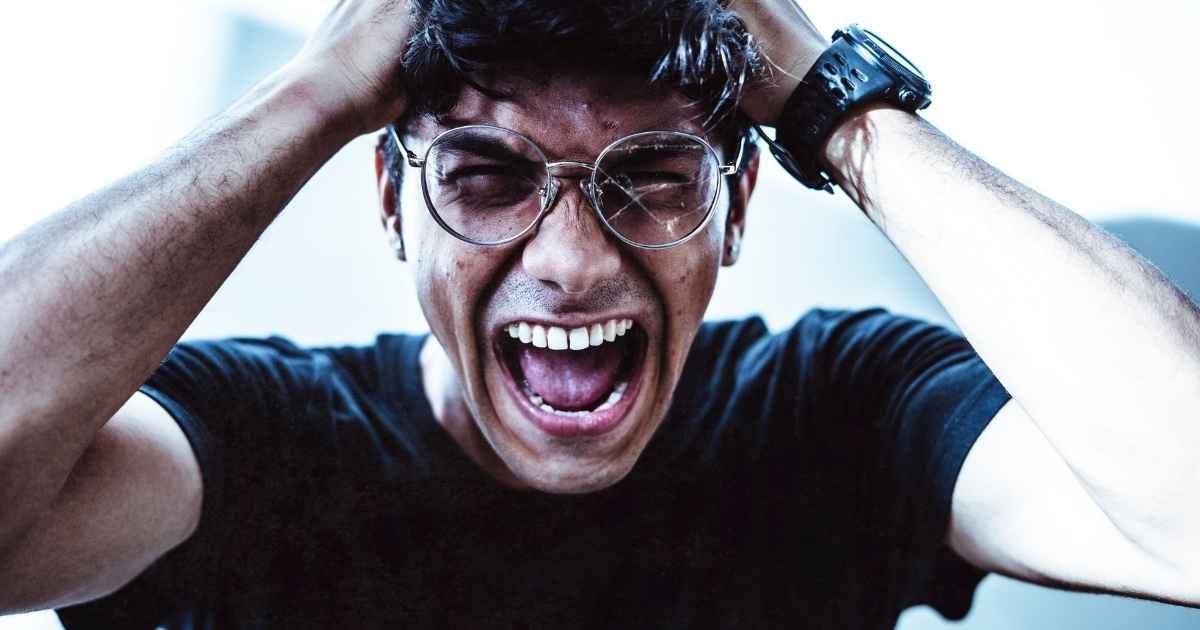 A close-up of a man shouting in frustration, clutching his head with broken eyeglasses on A close-up of a man shouting in frustration, clutching his head with broken eyeglasses on