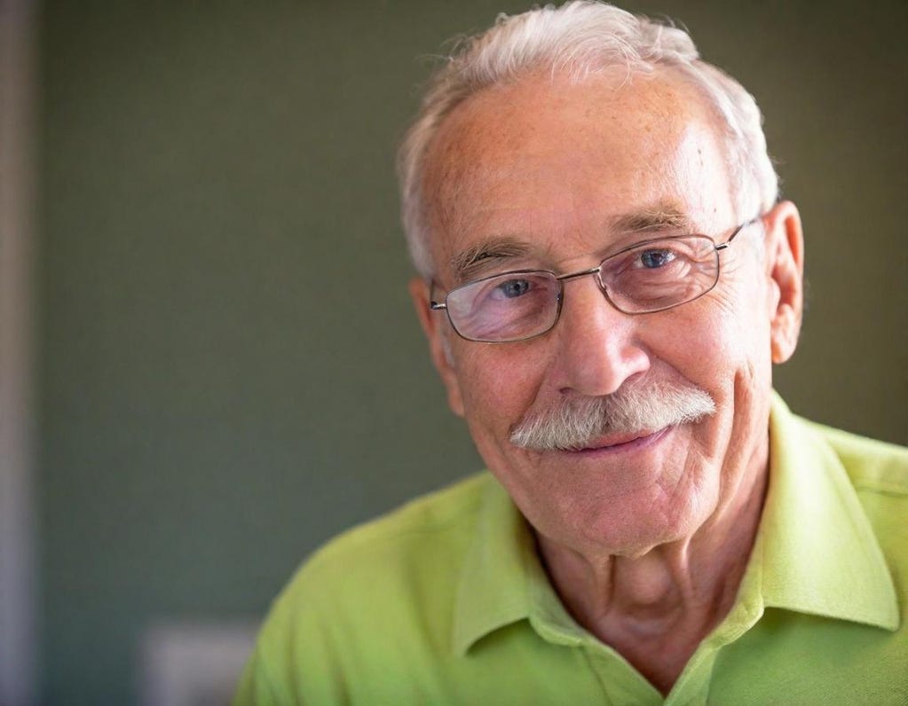 Tight portrait of 80-year-old grinning white man with mustache and glasses. He wears a green shirt. Tight portrait of 80-year-old grinning white man with mustache and glasses. He wears a green shirt.