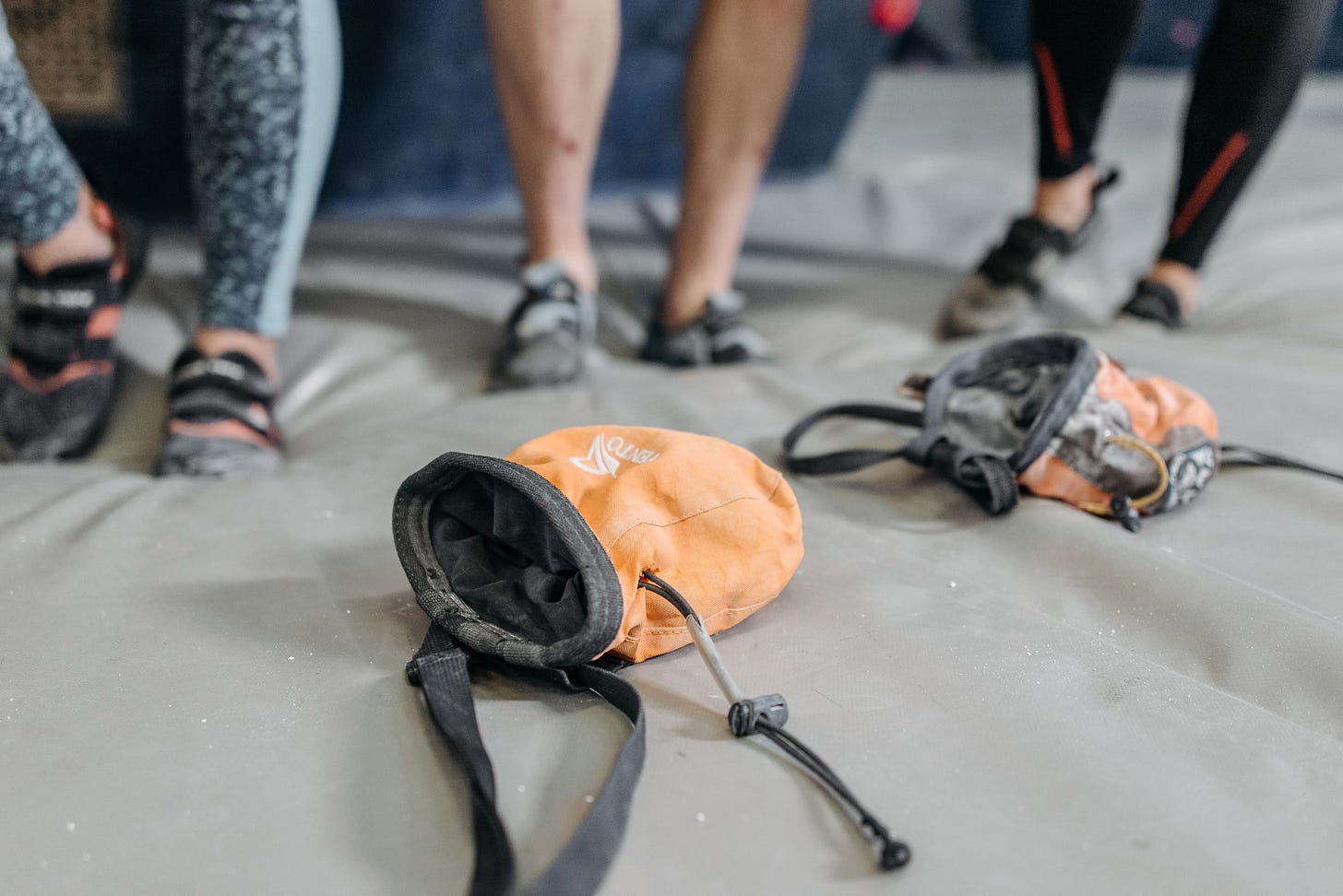 Man sieht die Beine von drei Boulderern im Hintergrund, während im Vordergrund zwei Chalkbags liegen. Man sieht die Beine von drei Boulderern im Hintergrund, während im Vordergrund zwei Chalkbags liegen.