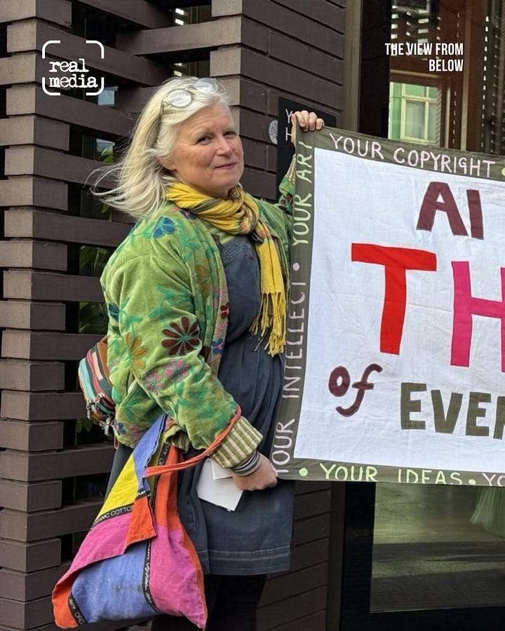 people stand outside office building holder a banner that reads "AI is the thief of everything"