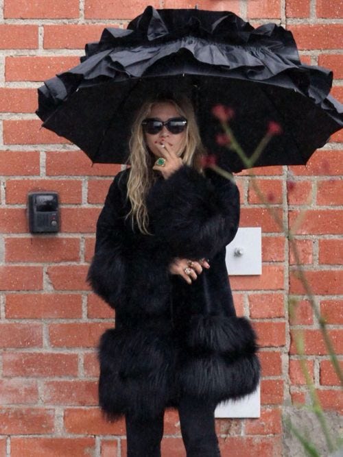 This may contain: black and white photograph of woman in fur coat holding an umbrella