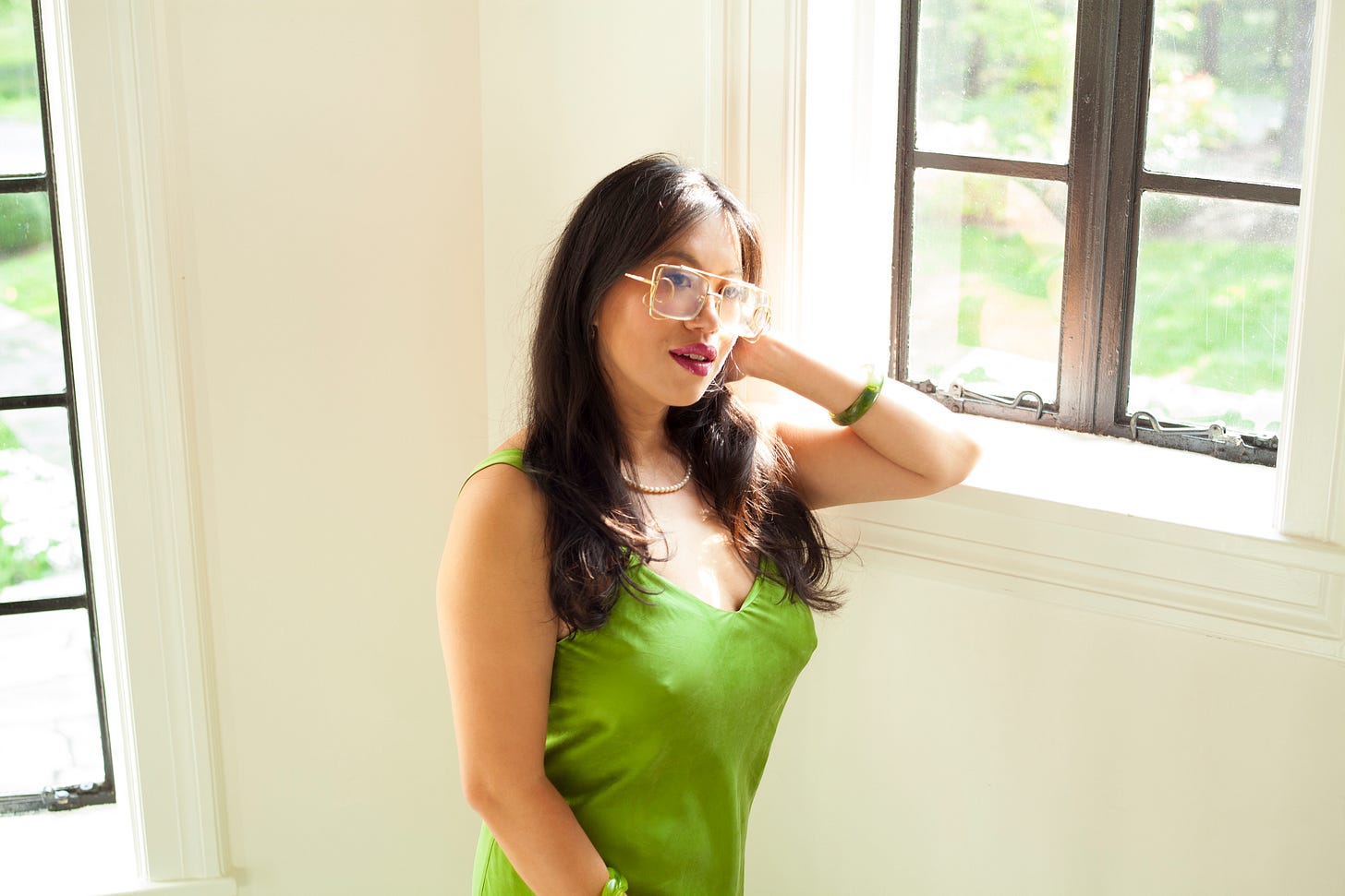 Image Description: Josie Qu is dressed in a body skimming green silk dress, her hand is pushing back her mid length black hair, and she is smiling into the camera
