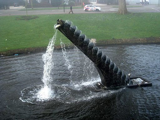 Sculpture of an Archimedes screw in a pond with a grassy bank around it and water gushing from the top back down in to the pond