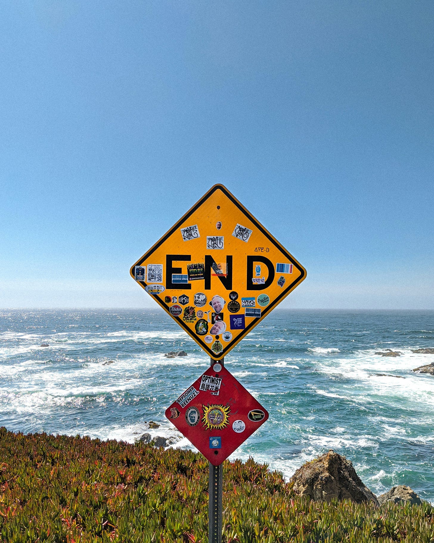 Photo of a street sign that says "end" overlooking a rocky beach. Photo of a street sign that says "end" overlooking a rocky beach.
