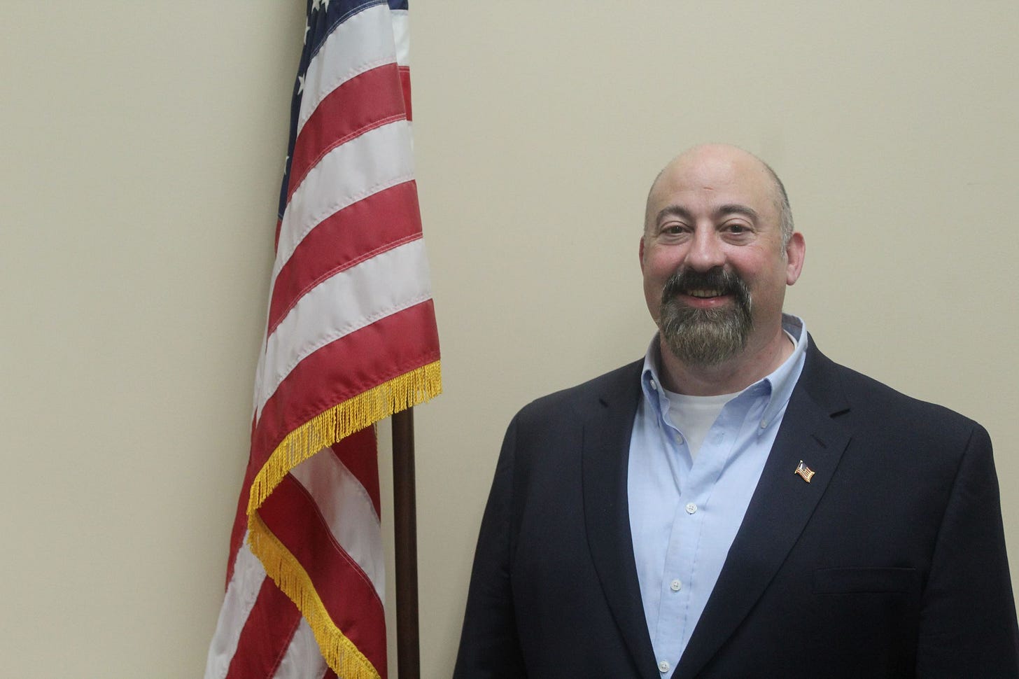 man in suit with shaved head by American flag