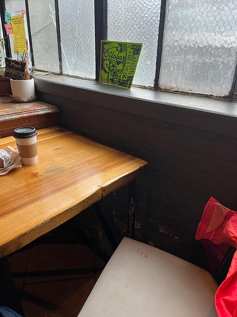 A black figurine of an Egyptian cat. A road lined with blossoming cherry trees. A necklace of aqua colored stones that are cracked and broken. An empty seat and rainy window at a cafe, with coffee on the table. An ikebana arrangement of tall daffodils. A campfire burning inside a potbellied chiminea. A collection of art supplies and a plaster angel. A watercolor sketch of cartoon spiders. A whiteboard at my job bearing the question, What's Your Favorite Thing About Baltimore In The Summer? With many many answers.