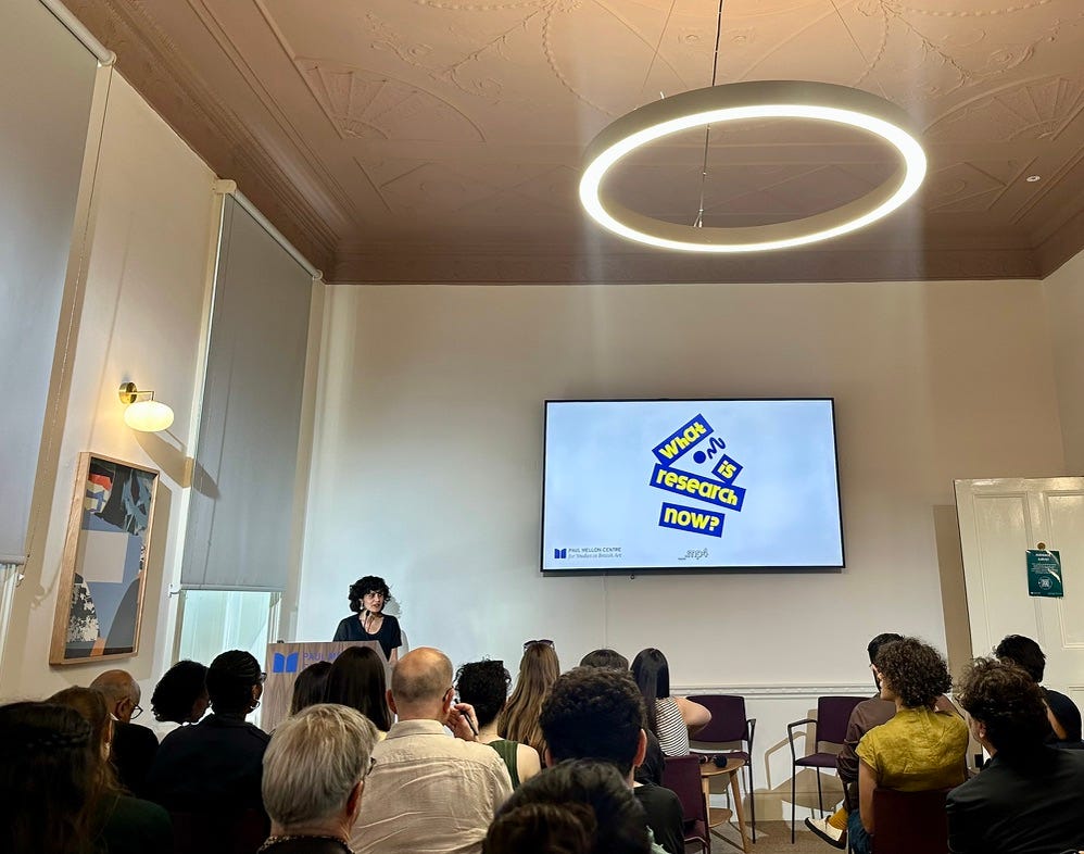 A South Asian woman speaking to an audience at an event called What Is Research Now? in a stylish conference eighteenth century Georgian-era room fitted out with modern amenities. A South Asian woman speaking to an audience at an event called What Is Research Now? in a stylish conference eighteenth century Georgian-era room fitted out with modern amenities.
