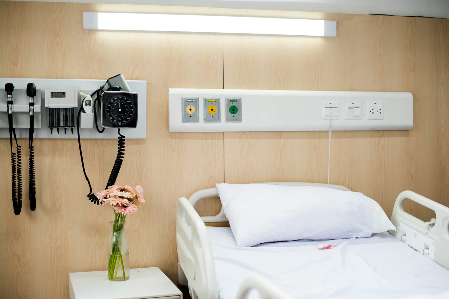 a hospital bed with a table beside it that has pink flowers in a vase