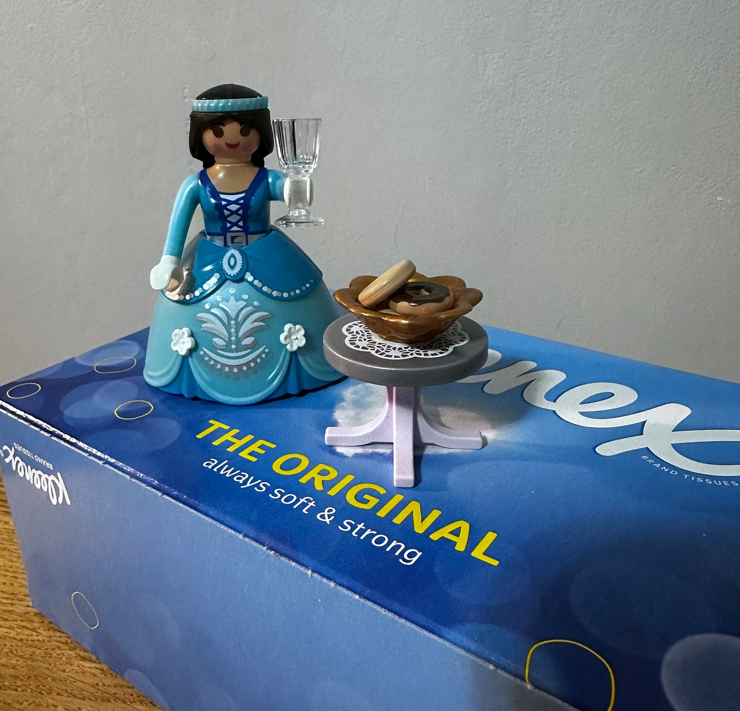 Image shows a Playmobil princess character holding up a glass and standing on top of a box of Kleenex