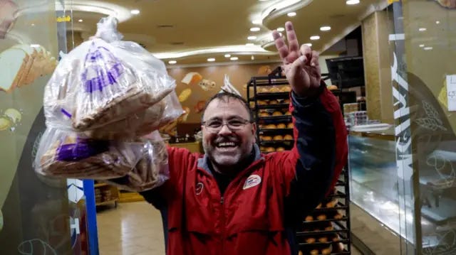 A man flashes the peace sign outside of a bakery A man flashes the peace sign outside of a bakery